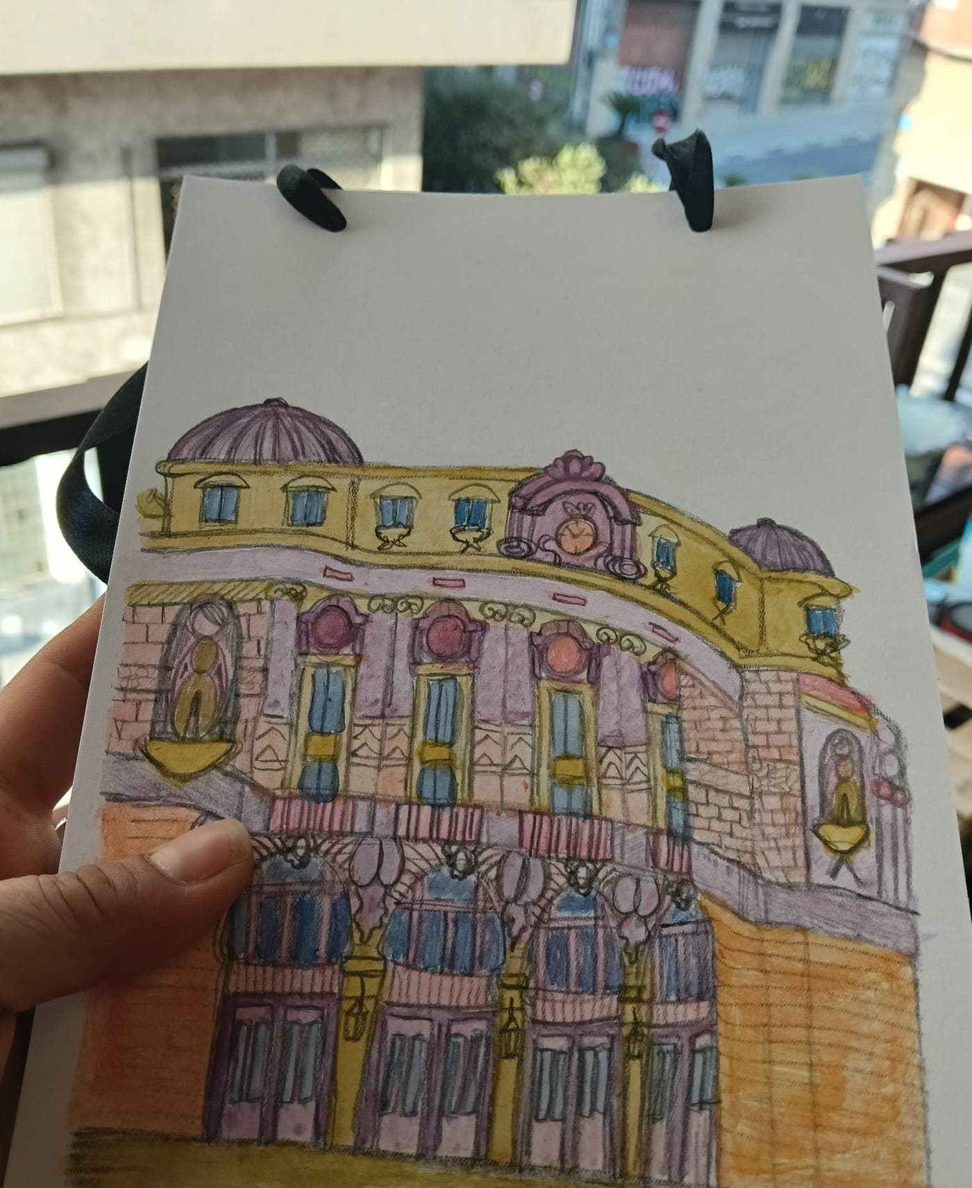 Ilustración coloreada de una fachada con cúpulas, sostenida en la mano